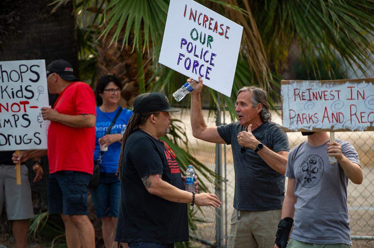 Adam Jordan, center, of the Anti Police-Terror Project, speaks to Jim Dobrinski, holding a sign calling for a larger police force, at two protests faced off on Broadway about police funding and homelessness Saturday.