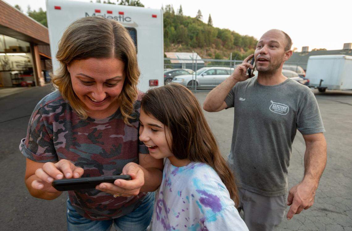 Amoreena and Matt Freitas, and daughter Maci, 9, react on Tuesday, Aug.17, 2021, after seeing a cell phone photo that shows their home on Tyler Drive in Grizzly Flats survived the Caldor Fire. The family evacuated to Placerville to camp out in the parking lot of Matt’s workplace.