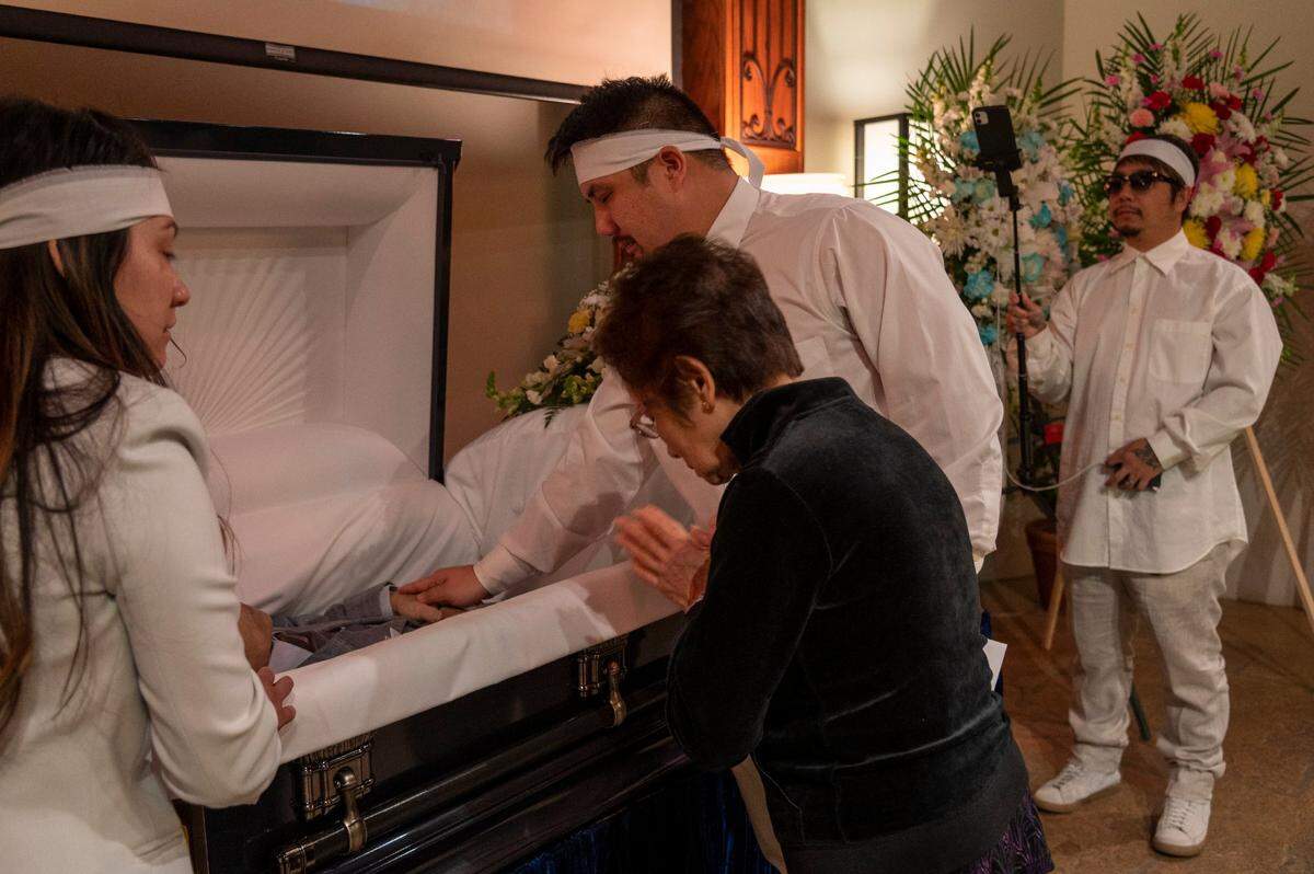 Bao Nguyen, right, records the funeral of his father Dung Tan Nguyen as his brother Michael Chonbon, second from right, gives one last touch while standing alongside Trang Nguyen, left, and Kim Anh Dinh, on Wednesday, May 6, 2020, during the coronavirus outbreak. Only four family members were permitted inside the funeral chapel and the family members were torn between grieving and taking turns holding the camera to live stream the service. Other mourners sat outside or in their cars trying to view the live stream but got frustrated because the video quality was bad.
