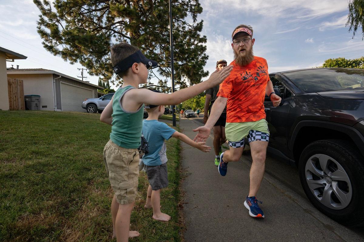 Caleb Broschat, captain of the Sloppy Moose Running Club, gets high fives from Johnathan, 7, and Logan Zagar, 4 as he jogs down Deerwood Street on June 20, 2024, at the backend of a three-mile jog that began and ended at Bike Dog Brewing Company in West Sacramento.