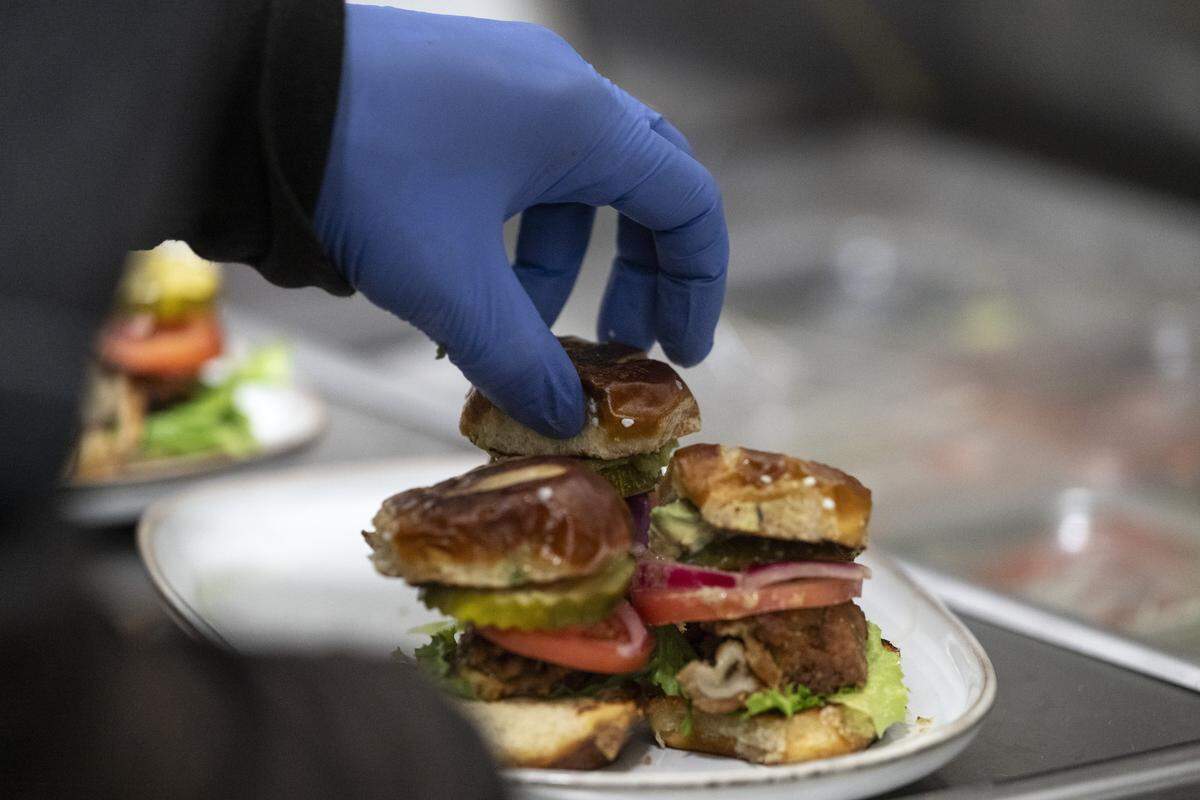 Elevated Eats owner Carlton Brown’s assistant, Rick, tops the oyster mushroom slider sampler with a pretzel bun at TAP Wine Lounge in Sacramento on Thursday, Dec. 4, 2025. Brown started the all-vegan business earlier this year and is currently cooking out of TAP Wine Lounge’s kitchen.