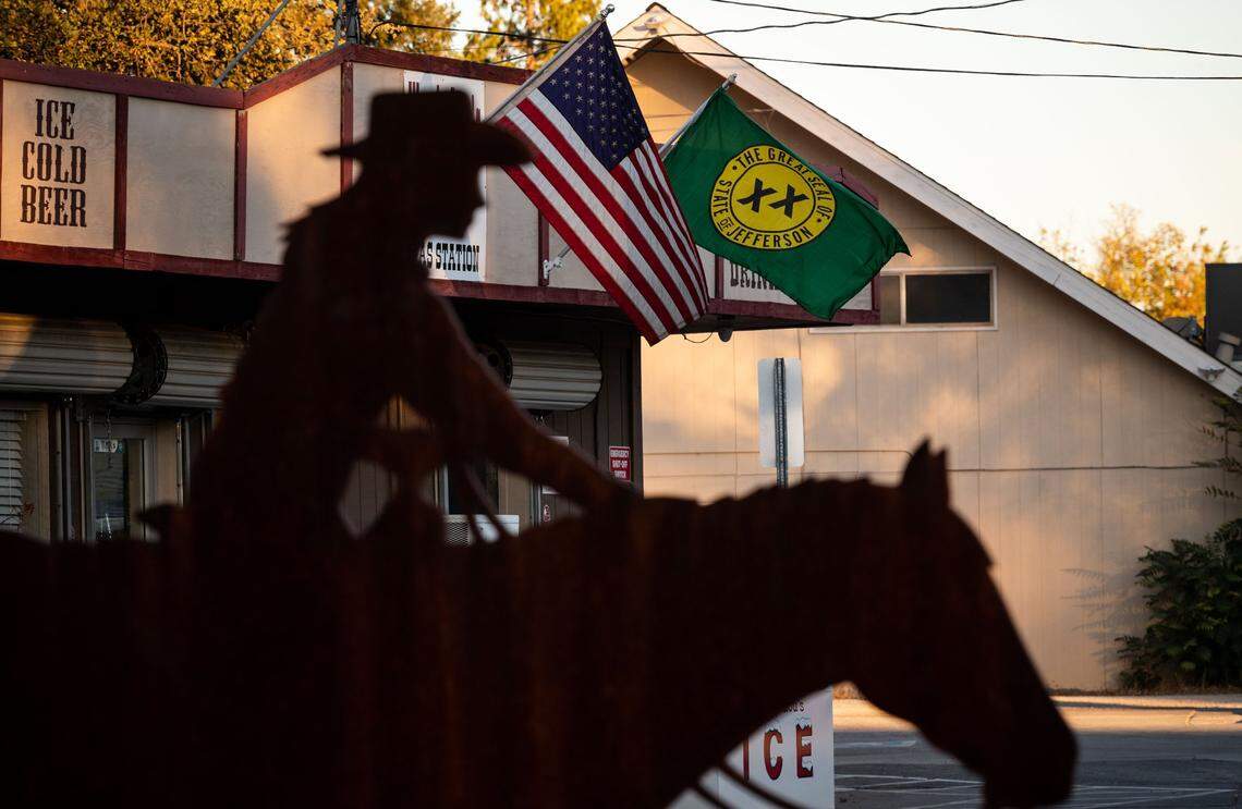 A flag which reads “The Great Seal of State of Jefferson” hangs next to a U.S. flag on a Main Street business, behind western-themed public art in the median, on Wednesday, Oct. 21, 2020, in the Shasta County community of Cottonwood.