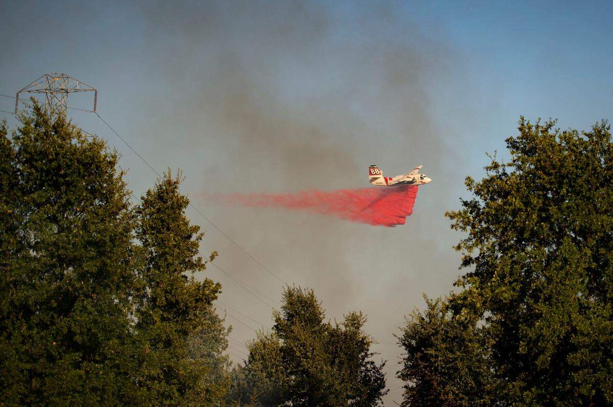 A Cal Fire plane drops fire retardant on a grass fire burning in the fields behind the Blue Oaks neighborhood of Roseville on Monday, Aug. 10, 2020.