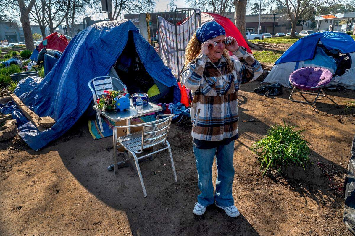 Dina Steffani, 53, wipes tears as she stands in front of her tent Friday near a small table with a flowering plant. “I pray every day for someone to stop and pick me up and take me home with them,” she said. “I don’t want to be out here no more.” The parcel of land where she camps near the corner of Fair Oaks Boulevard and Howe Avenue is owned by the City of Sacramento but the District Attorney’s Office and Sheriff’s Office appear to be preparing to file a lawsuit against the city over the encampment.