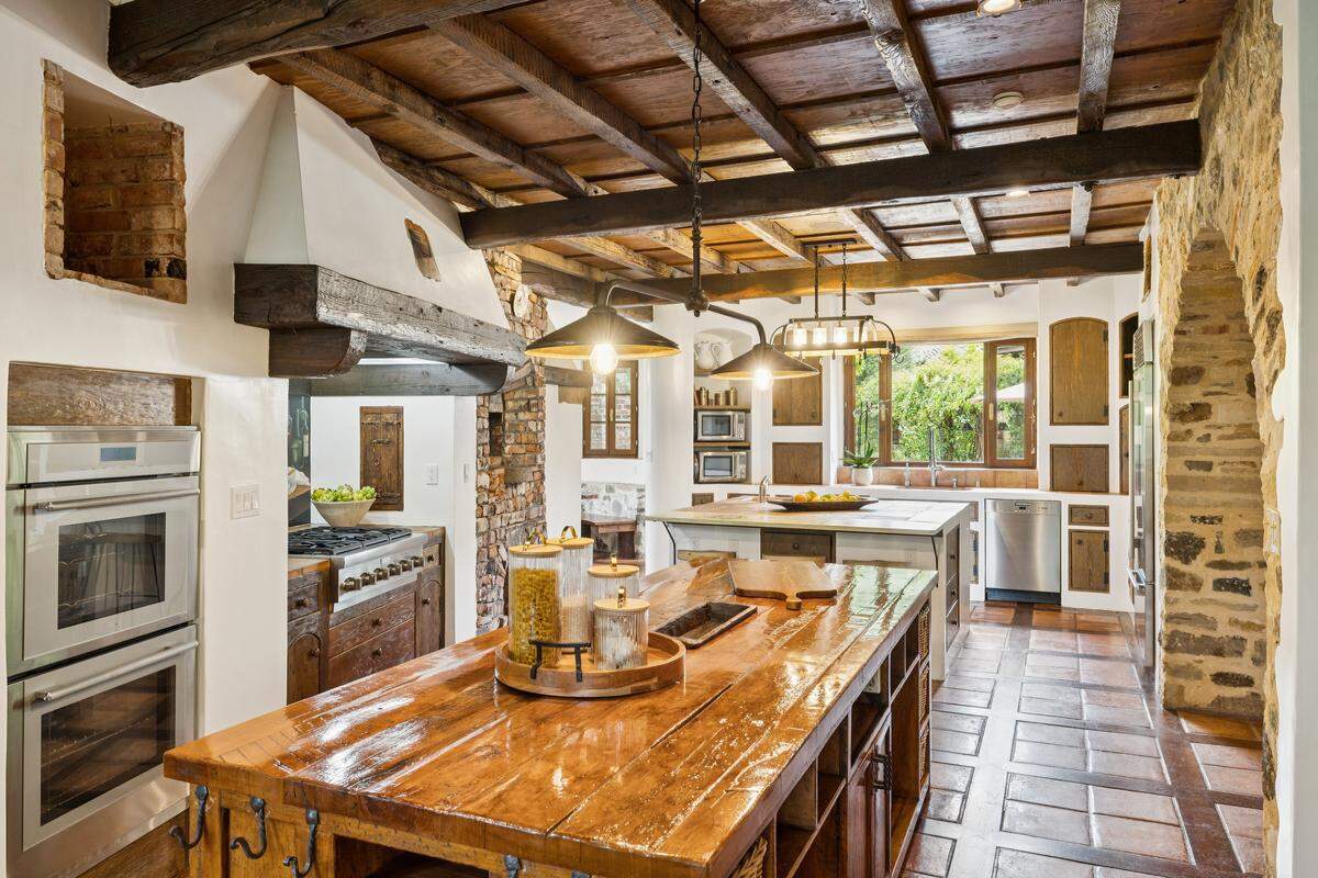 An expansive professional entertaining kitchen is appointed with doubles of necessary appliances for large gatherings, including grills and pizza ovens inside and out.