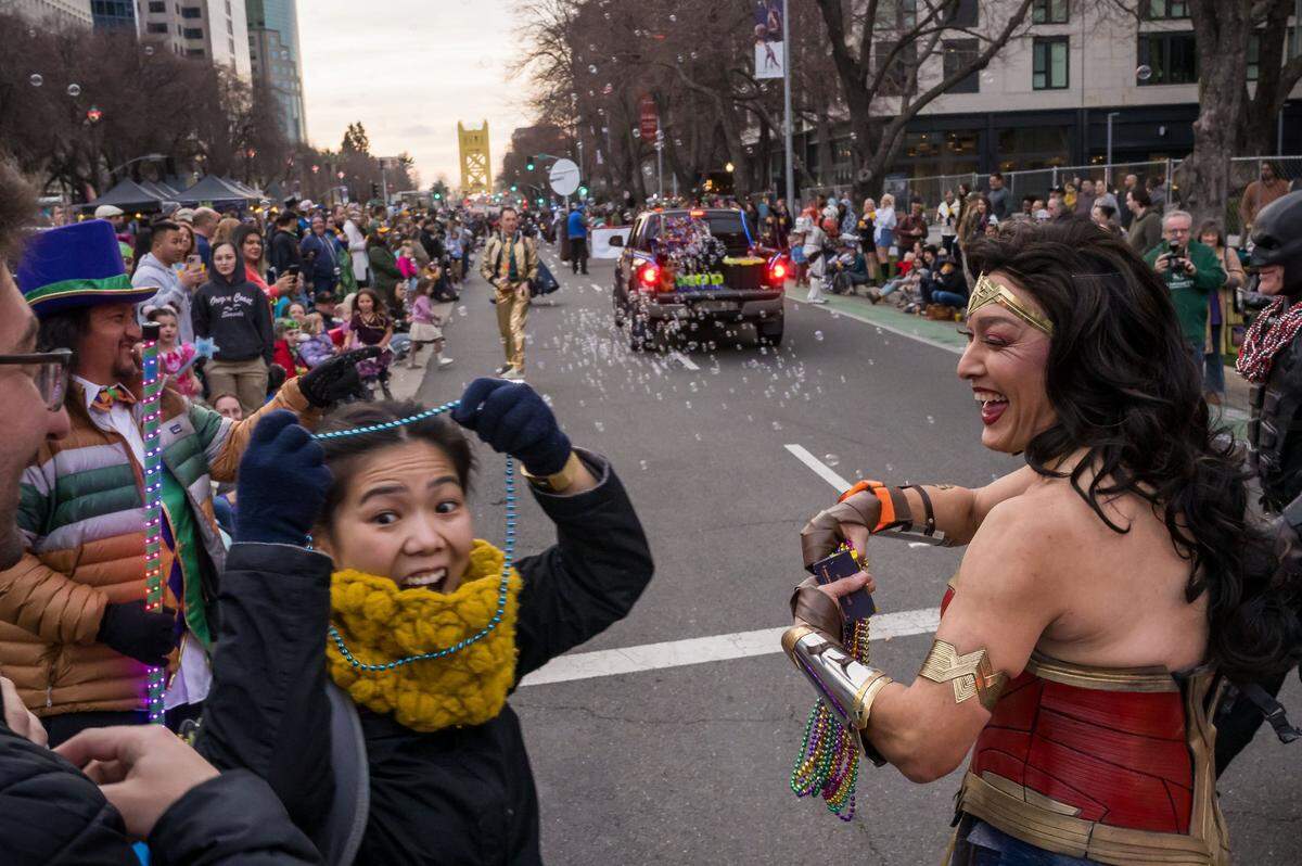 Kalani Makanani, right, with the League of Heroes Inspired, hands out beads while dressed as Wonder Woman during the City of Trees Parade Mardi Gras procession on Capitol Mall on Saturday, Feb. 18, 2023, in downtown Sacramento.