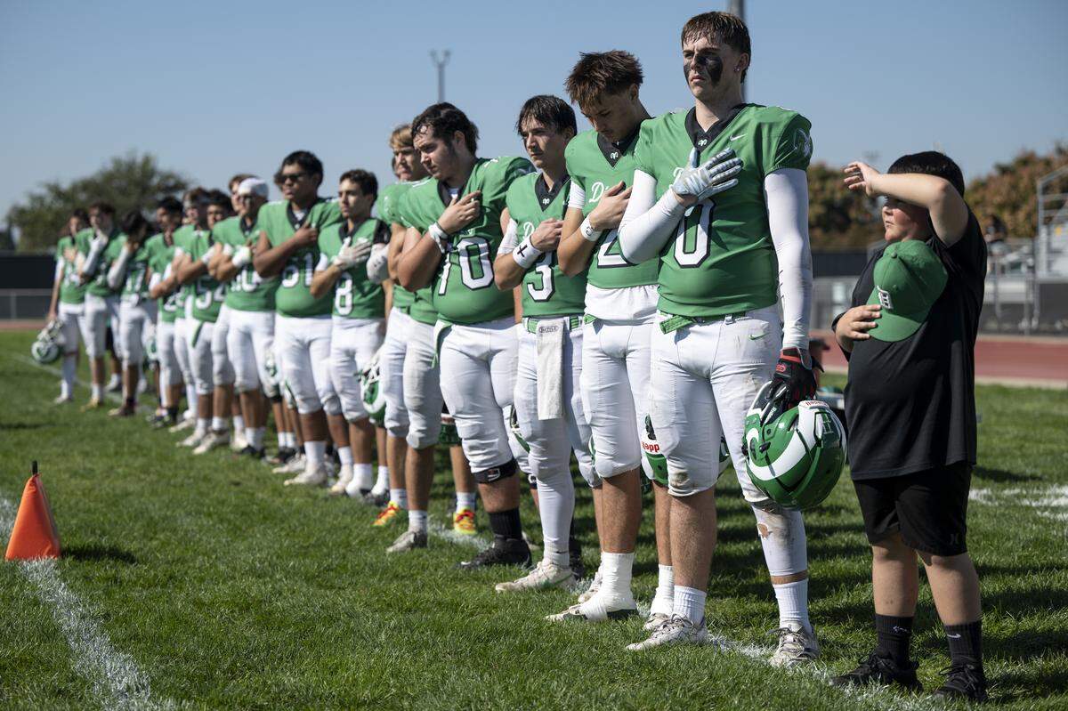 Dixon varsity football players stand for the national anthem following a moment of silence for teammate Isaac Arredondo before a game between Dixon and Casa Roble in Dixon on Saturday.