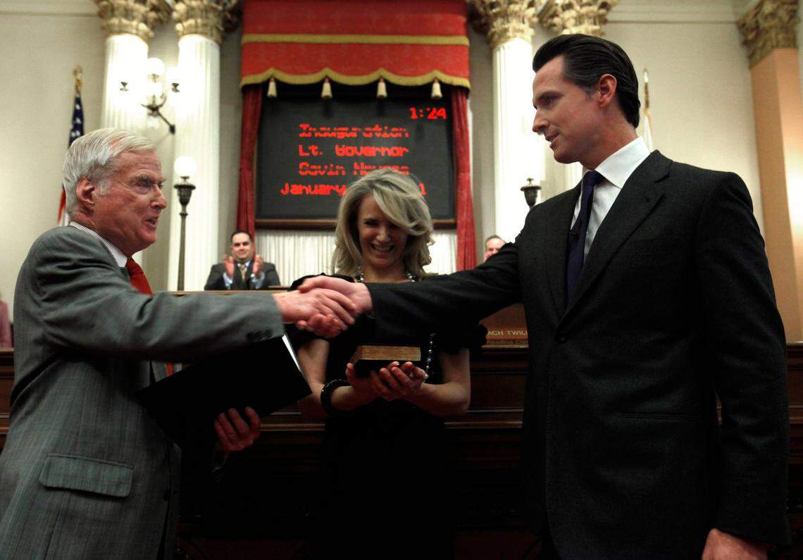 FILE - In this Jan. 10, 2011, file photo, Gavin Newsom, right, shakes hands with his father, William Newsom, a former Associated Justice of the California Court of Appeals, who swore his son into office as California’s 49th Lt. Governor, at the Capitol in Sacramento, Calif. Newsom’s wife, Jennifer Siebel Newsom is shown in the middle. William Newsom has died at age 84. A Gavin Newsom spokesman says William Newsom died Wednesday morning, Dec. 12, 2018, at his home in San Francisco.
