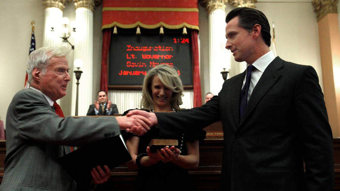 FILE - In this Jan. 10, 2011, file photo, Gavin Newsom, right, shakes hands with his father, William Newsom, a former Associated Justice of the California Court of Appeals, who swore his son into office as California’s 49th Lt. Governor, at the Capitol in Sacramento, Calif. Newsom’s wife, Jennifer Siebel Newsom is shown in the middle. William Newsom has died at age 84. A Gavin Newsom spokesman says William Newsom died Wednesday morning, Dec. 12, 2018, at his home in San Francisco. (AP Photo/Rich Pedroncelli, File)