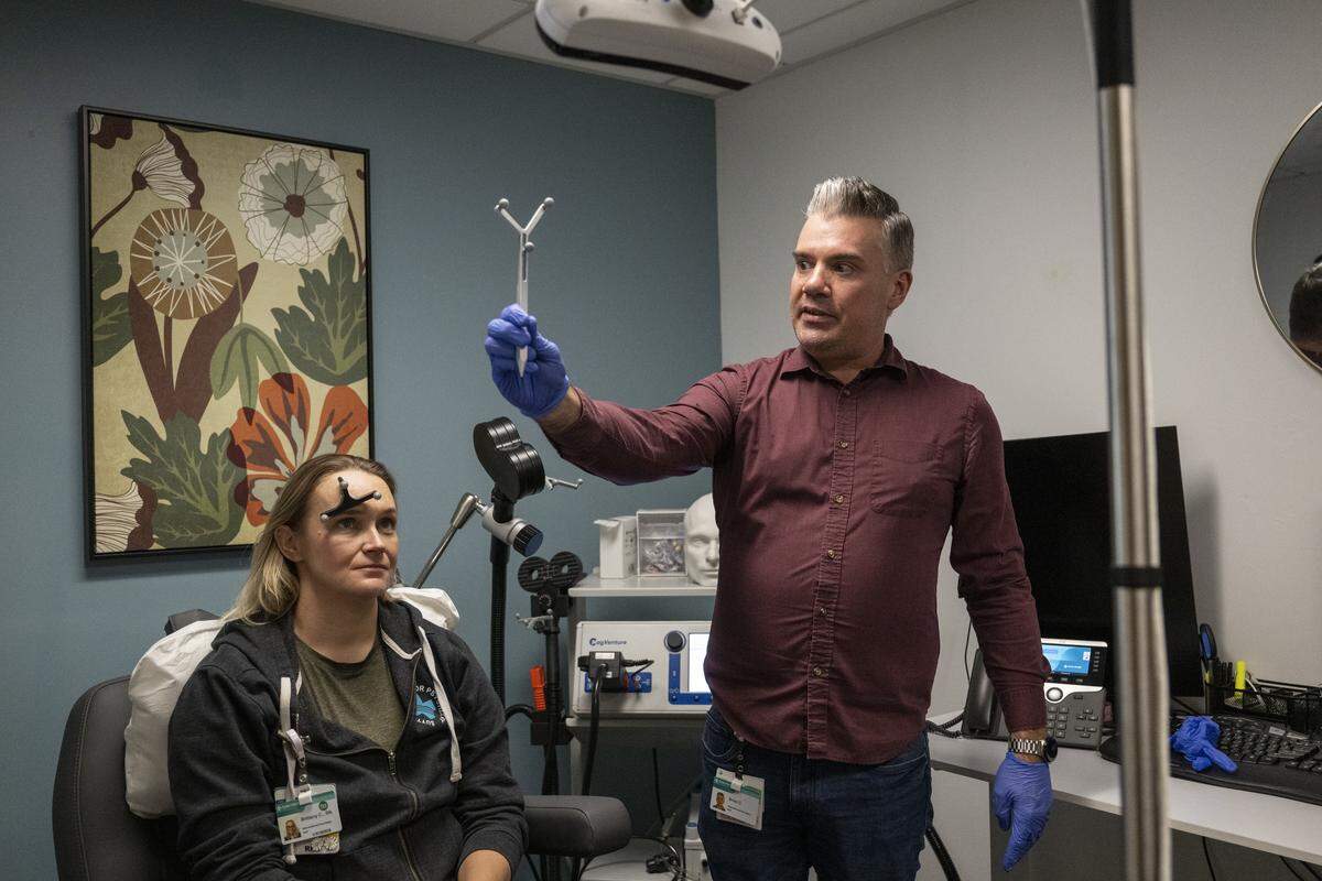 Brian Croom, a specialist at the Sutter Center for Psychiatry, demonstrates with Brittany Chik the setup for the SAINT transcranial magnetic stimulation treatment in Sacramento on Monday, Dec. 8, 2025. The treatment is designed to address treatment resistant depression in a shorter period of time.
