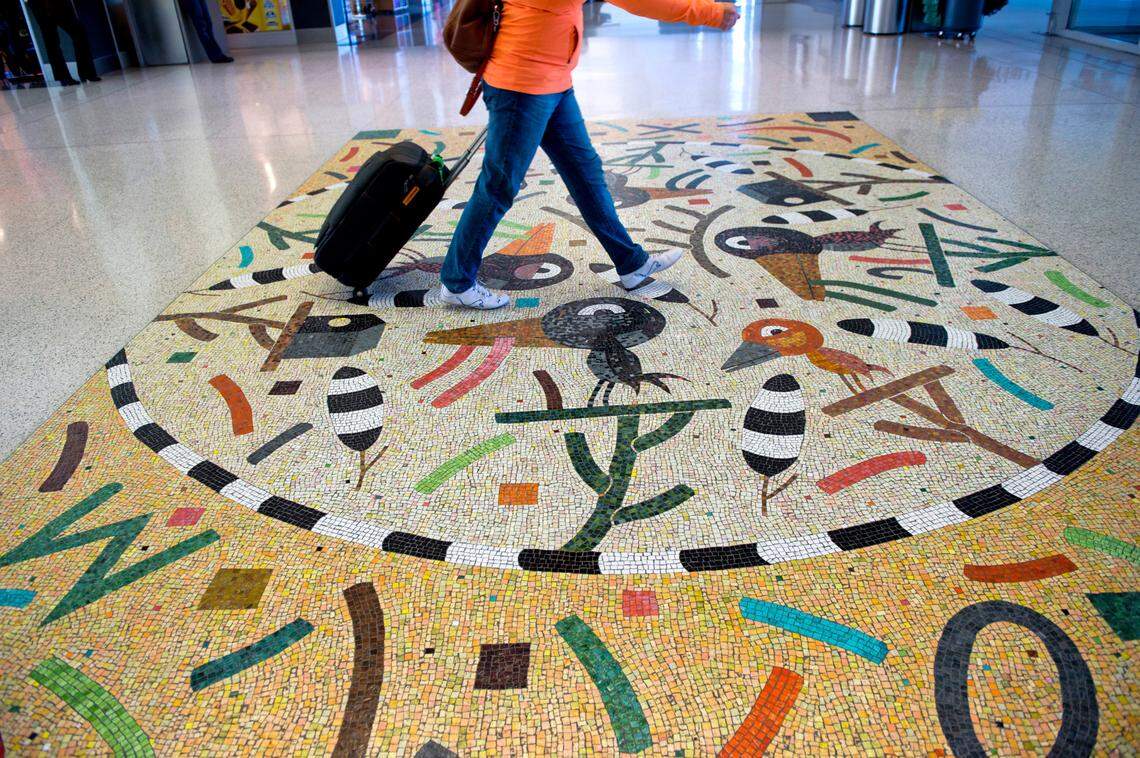 A passenger makes her way toward the automated people mover in Terminal B at the Sacramento International Airport on Dec. 12, 2013, in Sacramento. She walks across “Flying Colors,” a glass mozaic by Suzanne Adan.
