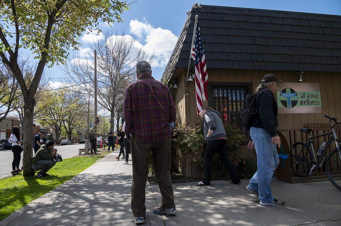 Customers line up outside of All about Wellness, a Sacramento medical cannabis dispensary, waiting for their orders to be fulfilled during the coronavirus pandemic on Thursday, March 19, 2020 in Sacramento.