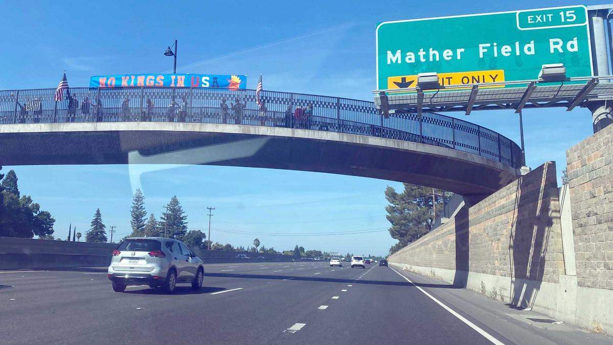 Protesters raise a banner saying “No Kings in USA” on a pedestrian overpass along Highway 50 near Mather Field Road in Rancho Cordova on Saturday, June 14, 2025. Protests are being organized at the California state Capitol in Sacramento as well as several other locations in the capital region.