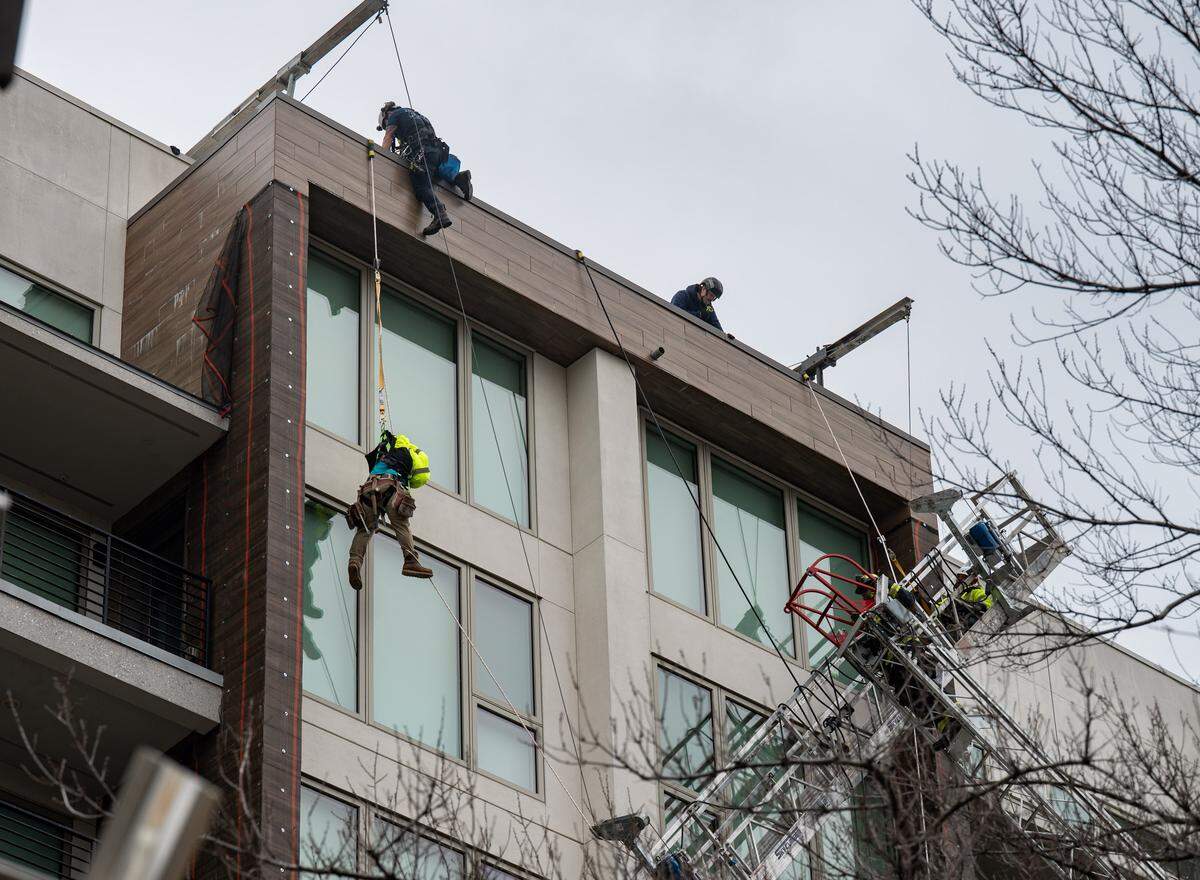 A Sacramento firefighter climbs over the parapet of a building at 15th and Q streets to rescue a dangling construction worker while a second worker awaits rescue in a hanging scaffold at far right on Wednesday.