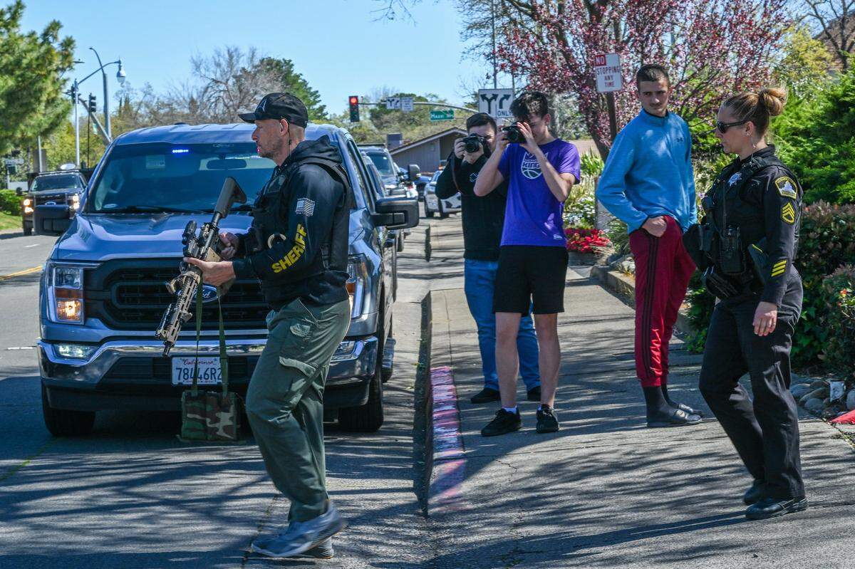 Officers return to their vehicle as bystanders watch during a standoff at the Hazel Ranch apartment complex in the 8800 block of Winding Way in Fair Oaks on Friday. They were retrieving water for other officers at the scene.