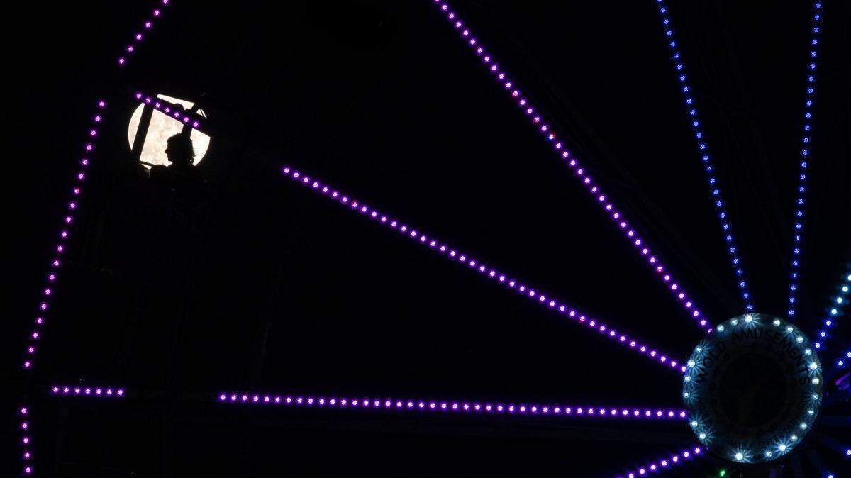 People ride the Wold Amusements Ferris wheel in view of the strawberry full moon Thursday, June 24, 2021, on opening night at the Placer County Fair in Roseville.