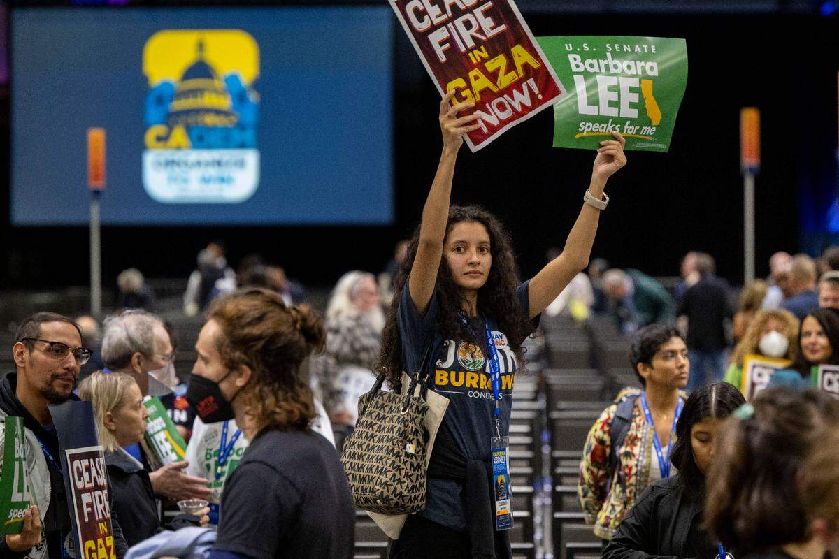 Annamarie Beltran of the Fresno County Young Democrats holds up signs calling for a cease-fire in the Gaza Strip as demonstrators march inside the session at the Democratic nominating convention Saturday at SAFE Credit Union Convention Center in Sacramento.