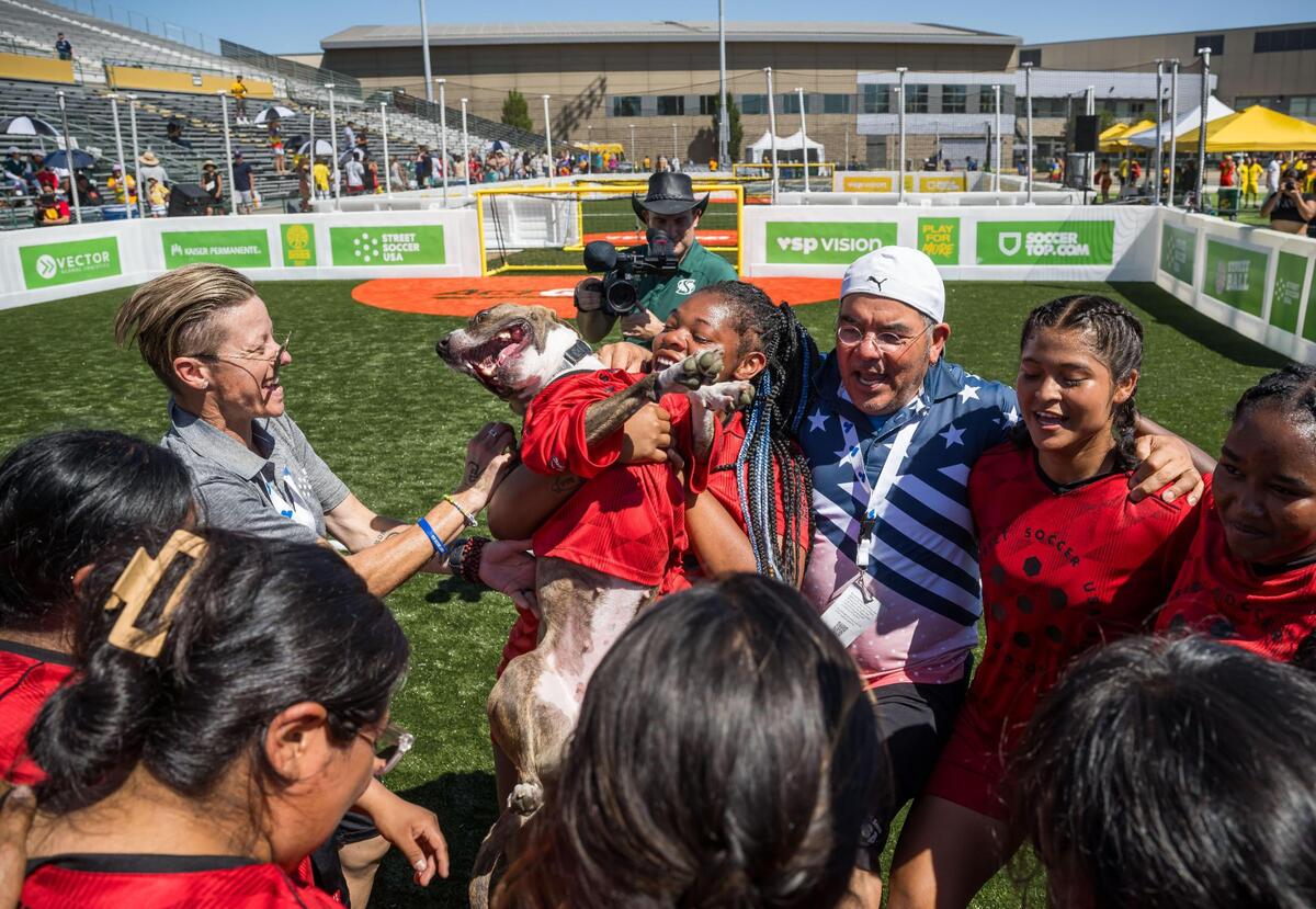 Lisa Wrightsman, a former player with the US women’s team and now Managing Director of the Sacramento Chapter of Street Soccer USA, left, celebrates with her players and April the dog after their win over Denmark during their match on the final day of the Homeless World Cup on Saturday, July 15, 2023, at Sacramento State’s Hornet Stadium.