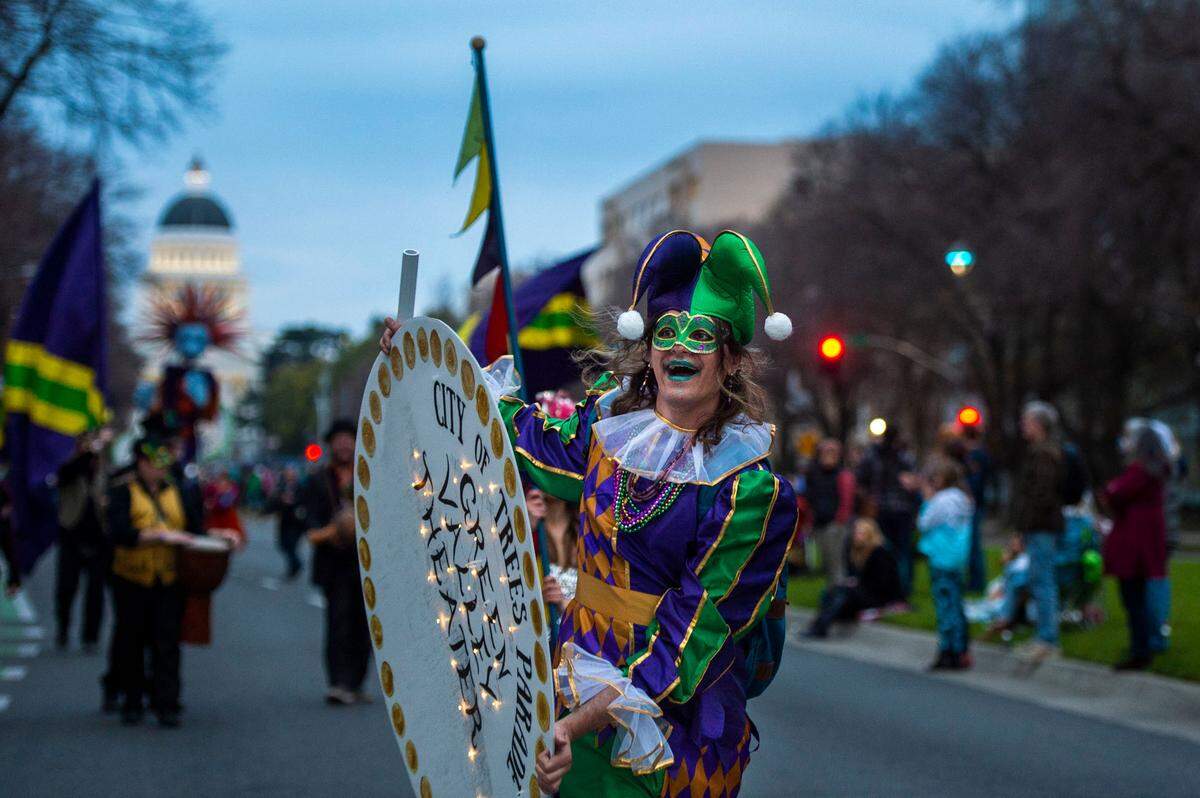 A performer with the Green Valley Theater dressed as a jester smiles at the crowd while walking down Capitol Mall during the City of Trees Mardi Gras parade on Saturday, Feb. 26, 2022, in downtown Sacramento.
