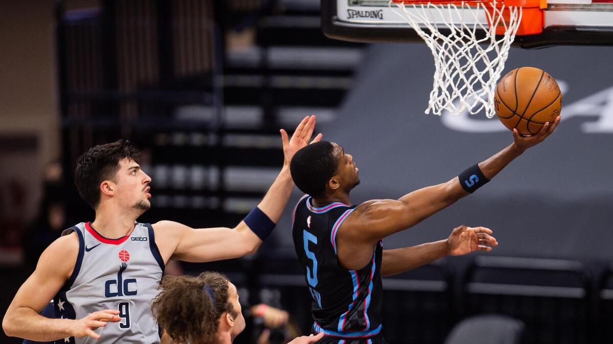 Sacramento Kings guard De’Aaron Fox (5), right, goes under the basket for layup past Washington Wizards forward Deni Avdija (9), left, and Washington Wizards center Robin Lopez (15) during the second period of the NBA game Wednesday, April 14, 2021, at Golden 1 Center in downtown Sacramento.