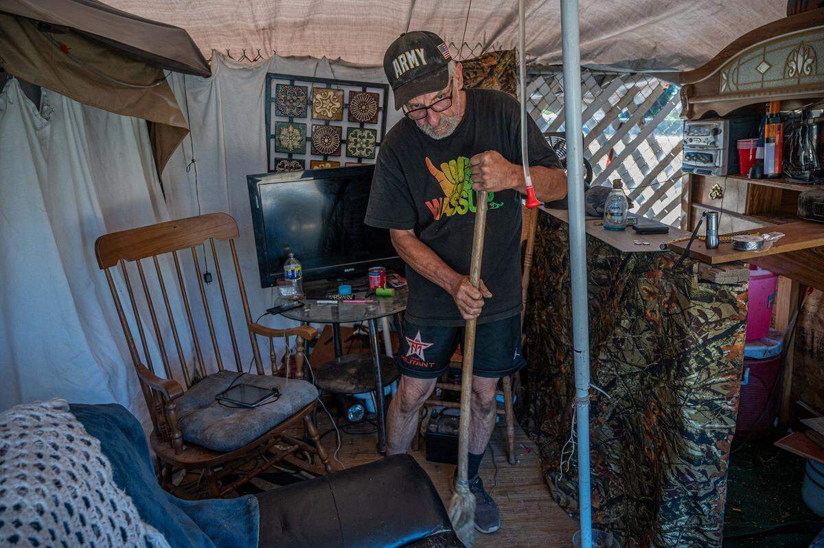 Carl White, 60, sweeps up the inside of his tent Thursday in Sacramento after restoring his broken bar and toppled furniture from a wind storm.