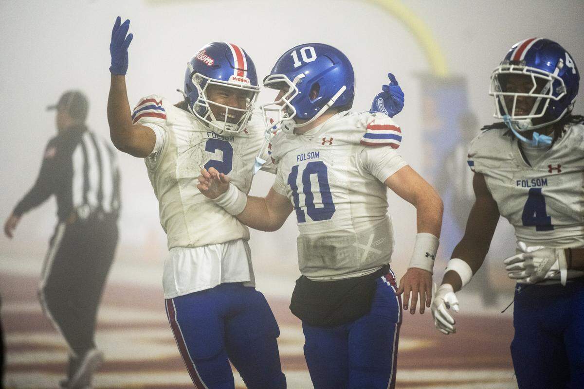 The Folsom Bulldogs' Brody Rudnicki (10) celebrates with teammates Jameson Powell (2) and Isaiah Williams (4) after scoring a touchdown in the second half against the Cathedral Catholic Dons in the CIF Division 1-AA State Championship football game at Saddleback College in Mission Viejo on Friday.
