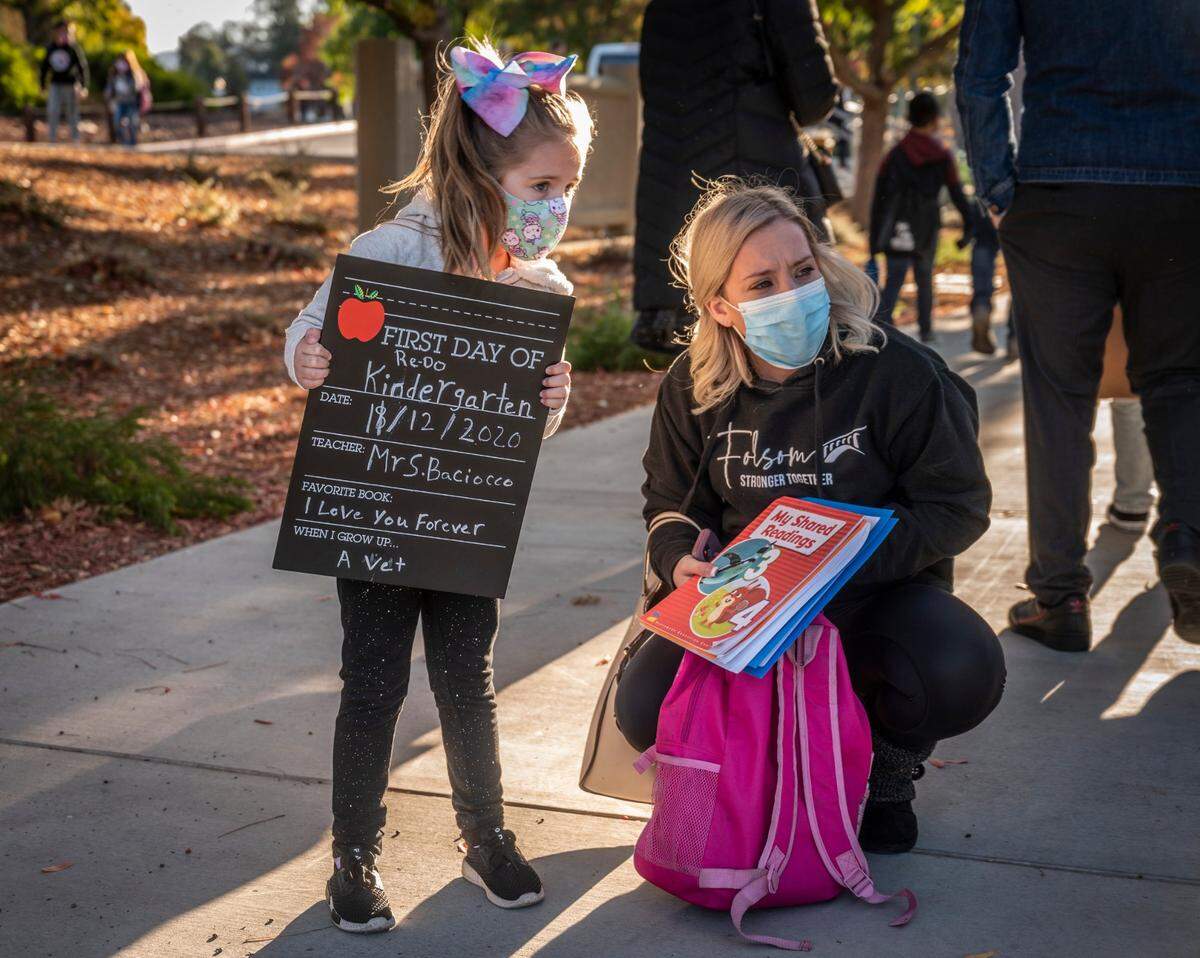 Paisley Murphy, 5, stands outside Folsom Hills Elementary School holding a chalkboard sign that says “First Day of Re-Do Kindergarten” with her stepmother Brittany Murphy on Thursday, Nov. 12, 2020. It was the first day of in-class instruction for elementary schools in the Folsom Cordova Unified School District since they closed in March amid the coronavirus pandemic.