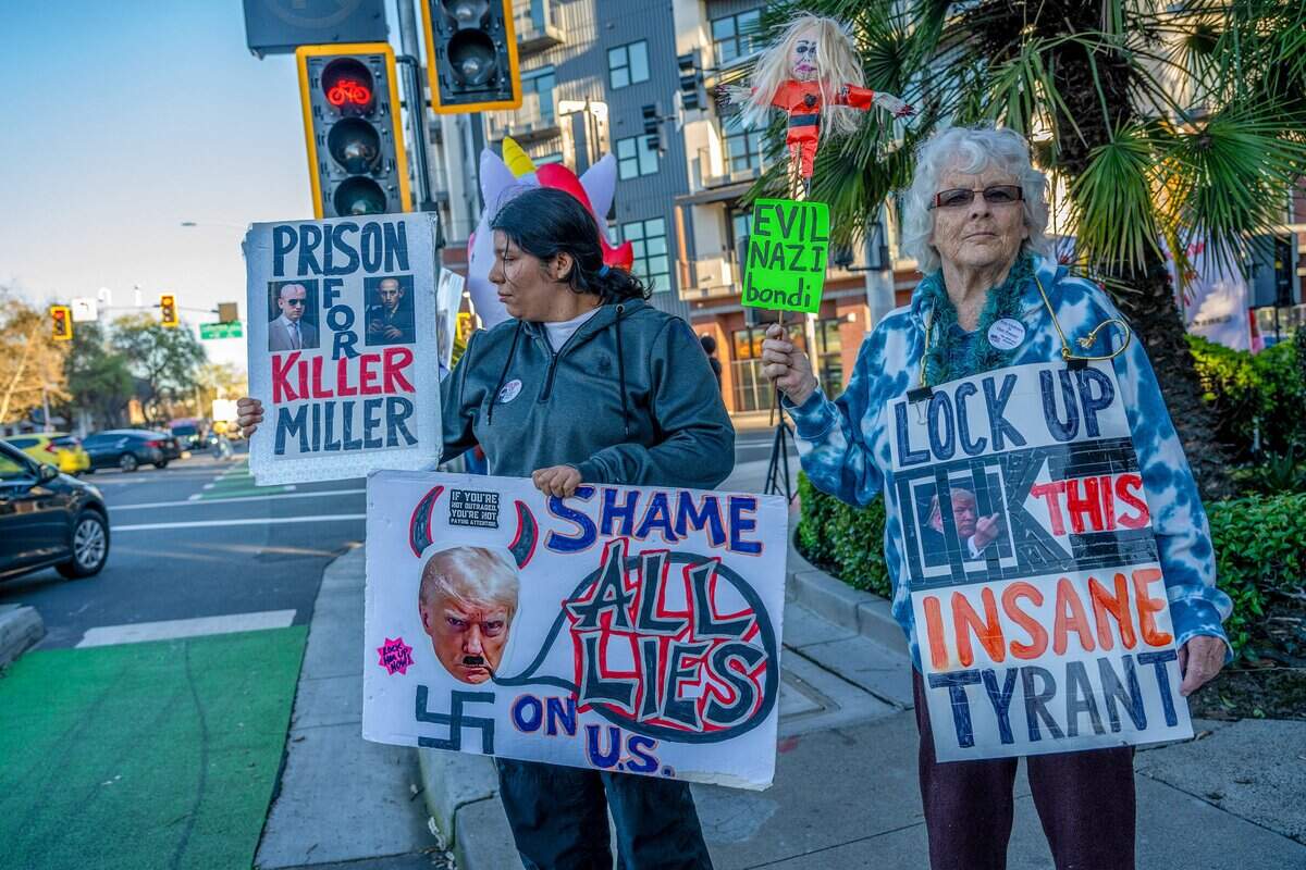 Yasmine Flores, left, and Deborah Earl, right, hold signs while attending a demonstration Monday at the intersection of 16th Street and Broadway in Sacramento against the U.S.-Israel war with Iran.