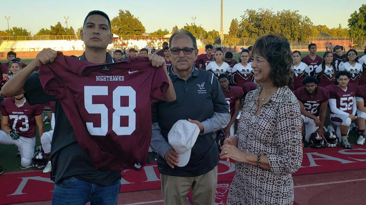 Richard Heredia-Arriaga displays his brother’s old Natomas High jersey while standing next to his dad, Salvador Arriaga, and mom, Susan Heredia, during a ceremony Friday.