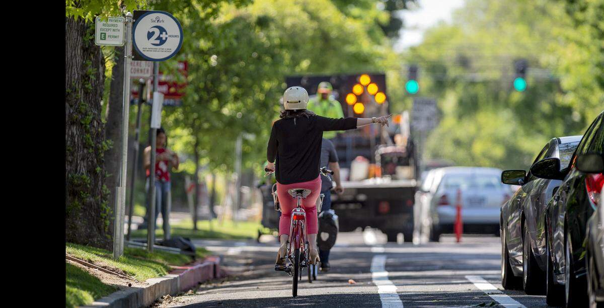 Jennifer Donlon Wyant, an active transportation program specialist with the city of Sacramento, makes a right turn signal while filming a video for the city of the new bike lanes at 13th and P streets on May 4. The bike lanes hug the curb between cars parked to the right.