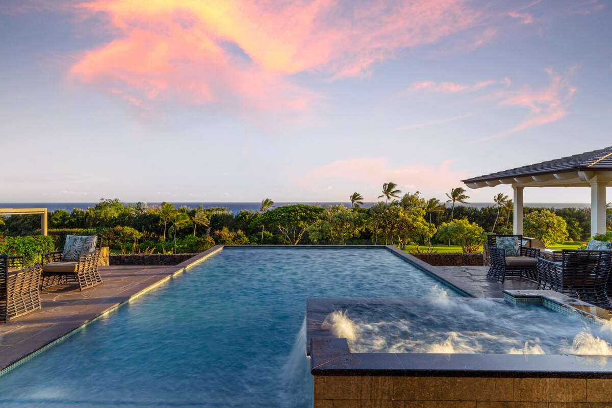 The terraced backyard includes a stunning pool and jacuzzi, outdoor kitchen, firepit, and one of Kukui’ula’s rare private pickleball courts, all overlooking ocean and golf course vistas in Kauai, Hawaii.