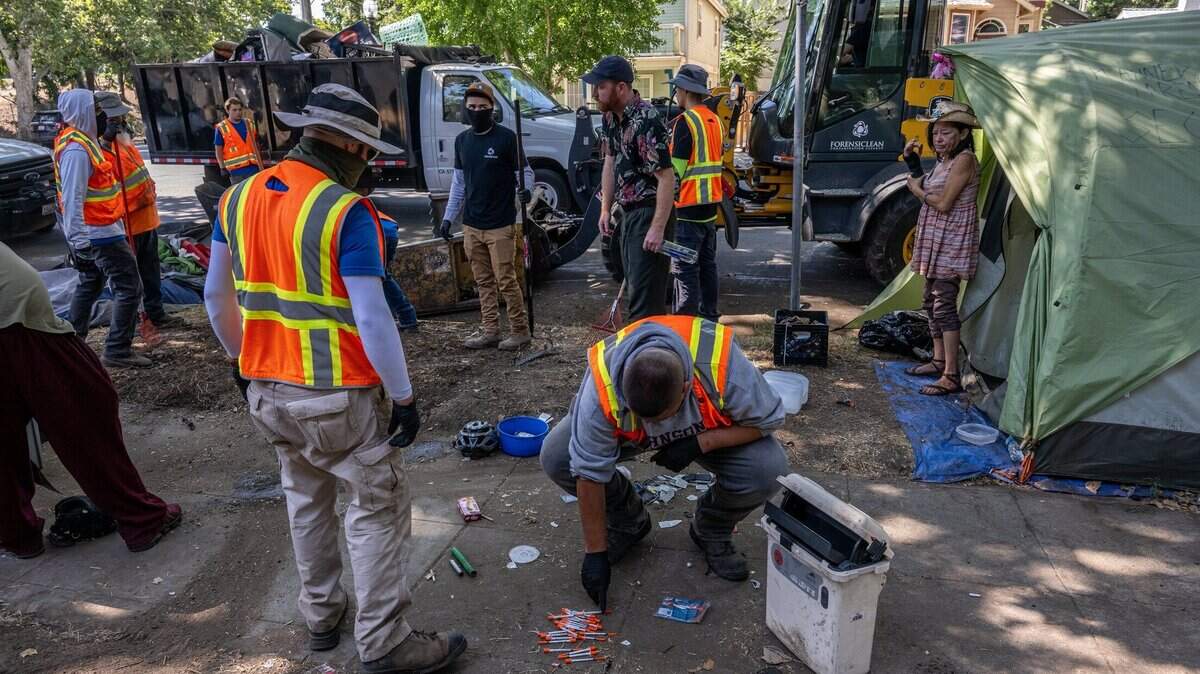City workers dispose of syringes homeless camper Alicia Peterson, 55, right, who said she was suffering from neuropathy and a wrist injury, looks on at a homeless encampment sweep at 28th and C streets in Sacramento on Wednesday, July 19, 2023.