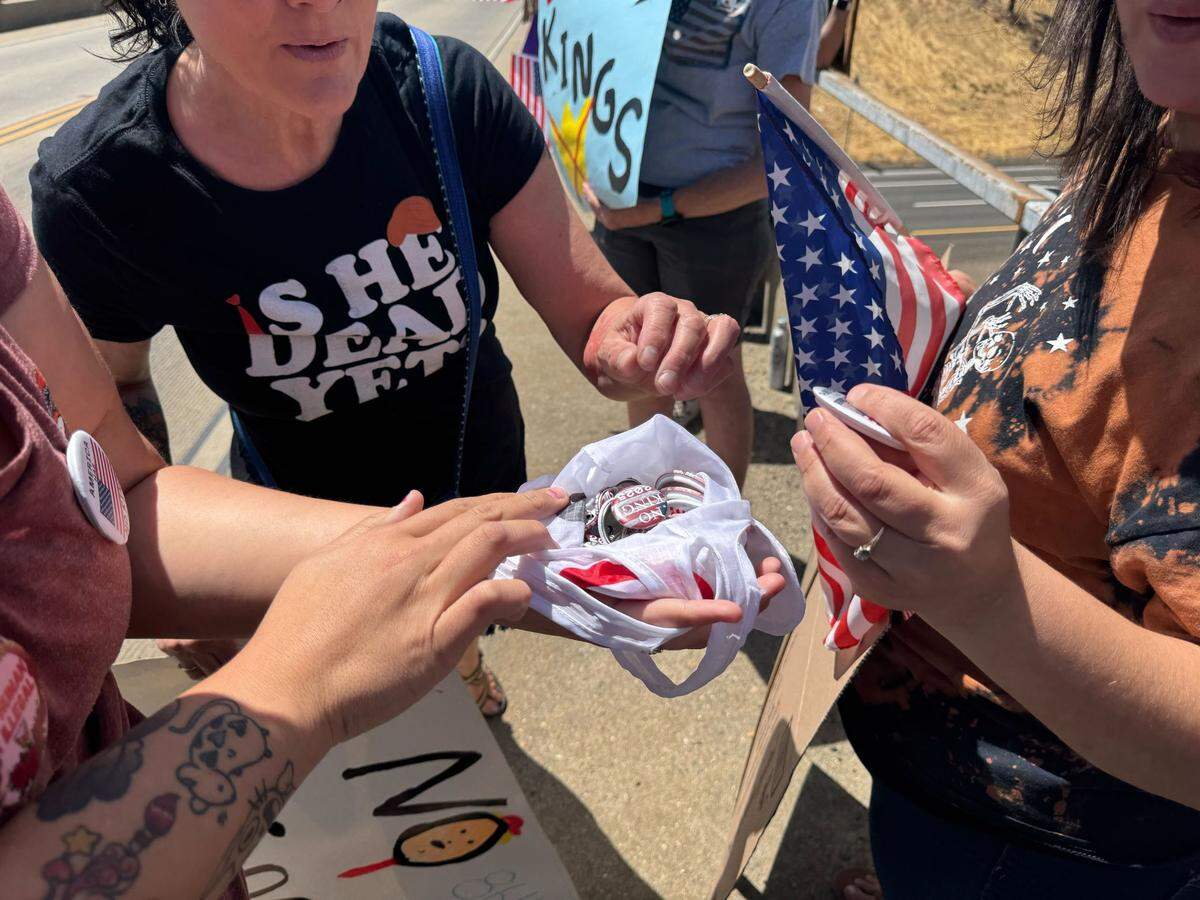 At the El Dorado Rd. Overpass near Diamond Springs and Placerville, Jacinda Tayaba hands out ‘No Kings’ buttons to fellow protesters carrying American flags.