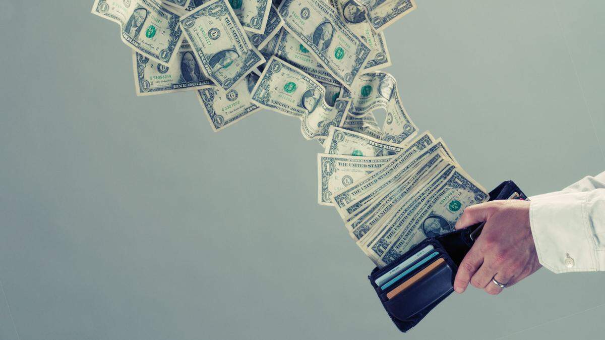 Man’s hand holding wallet while many bills fly out