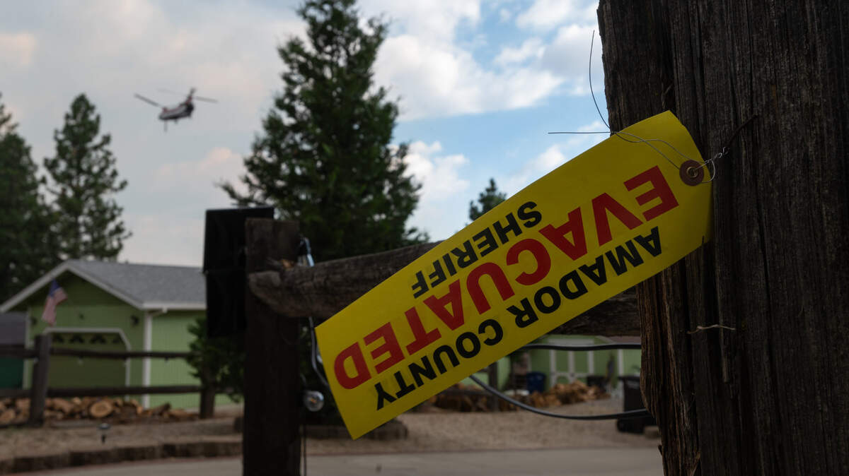 A tag from the Amador County Sheriff’s Office indicates that the residents of a home have evacuated inside the mandatory evacuation zone for the Electra Fire in Pine Grove on Tuesday evening, July 5, 2022, as a Chinook fire fighting helicopter flies above the threatened structures.