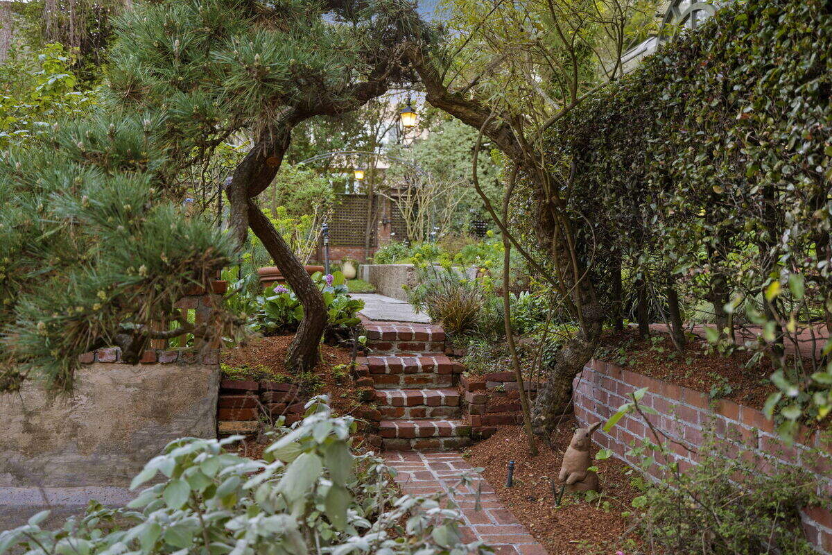 Multiple terraced levels step down into a lush, landscaped retreat, layered with mature trees and greenery, meandering paths and a fountain and pool.