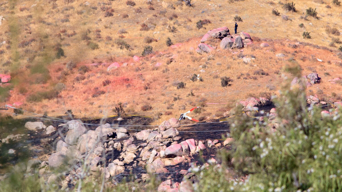 An investigator examines the hillside area Monday, Aug. 7, 2023, amid wreckage of the contract Cal Fire helicopters that collided on Sunday evening, killing three on one of the aircraft, in Cabazon, Calif.