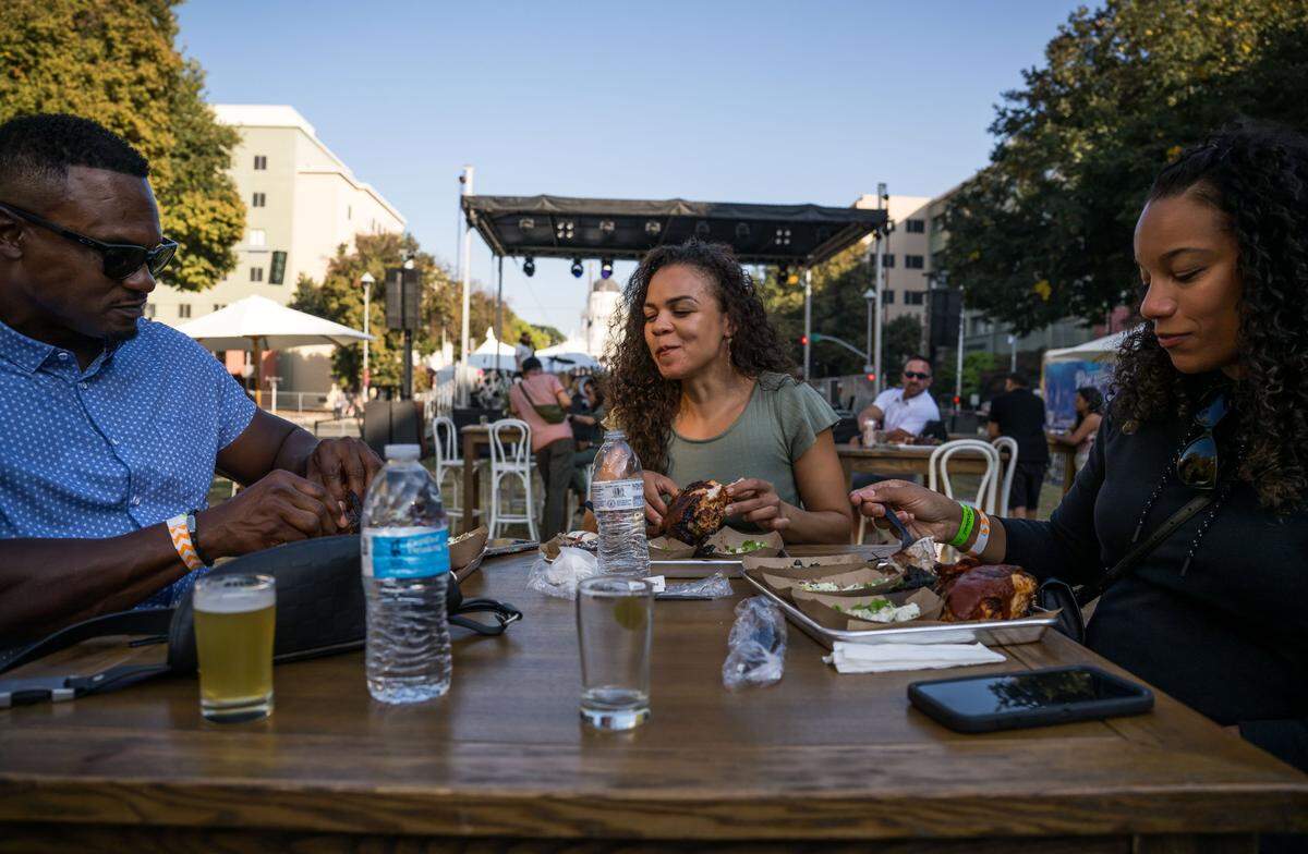 Teresa Mallory, center, takes a bite of barbecue chicken as she dines with friends Reginald Fulford, left, and Janine Reed, all of Sacramento, at the Farm-to-Fork Festival on Saturday, Sept. 23, 2023, on Capitol Mall in downtown Sacramento. The trio ate food prepared during Food Network’s Tyler Florence’s ticketed event with other local chefs featuring barbecue, craft beers and performances by Lindsay Ell and local artists Amador Sons and DJ Oasis.