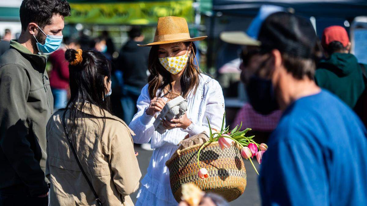 Marisa Minasian, of Sacramento, 38, middle, holds a carton of eggs at the Certified Farmer’s Market in the parking lot of Arden Fair mall in Sacramento on Sunday, March 21, 2021. It was the first day of the temporary relocation of the popular farmer’s market from under the W-X freeway because of road construction.