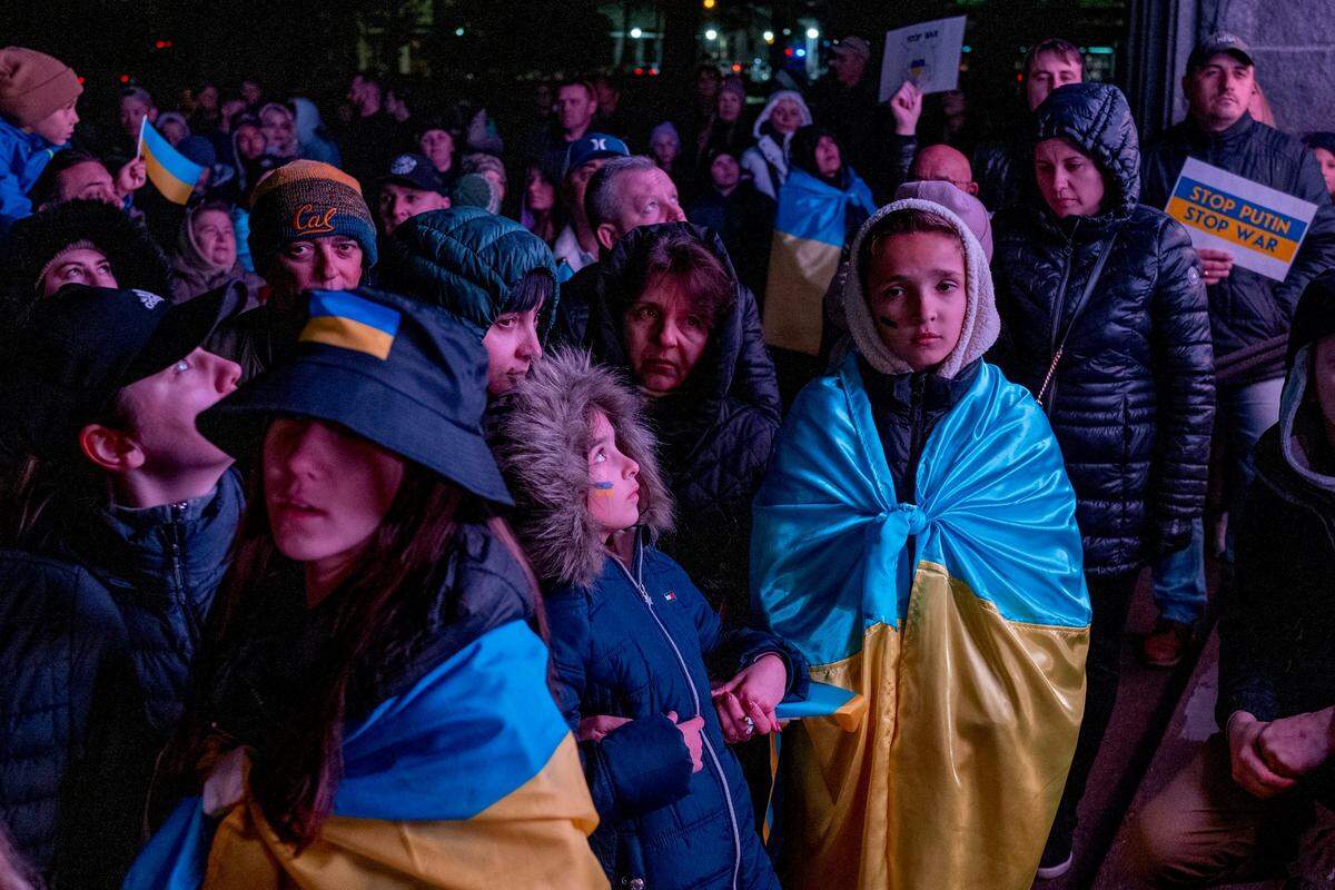 People draped in Ukrainian flags watch images from the war in Ukraine at the state Capitol on Friday.