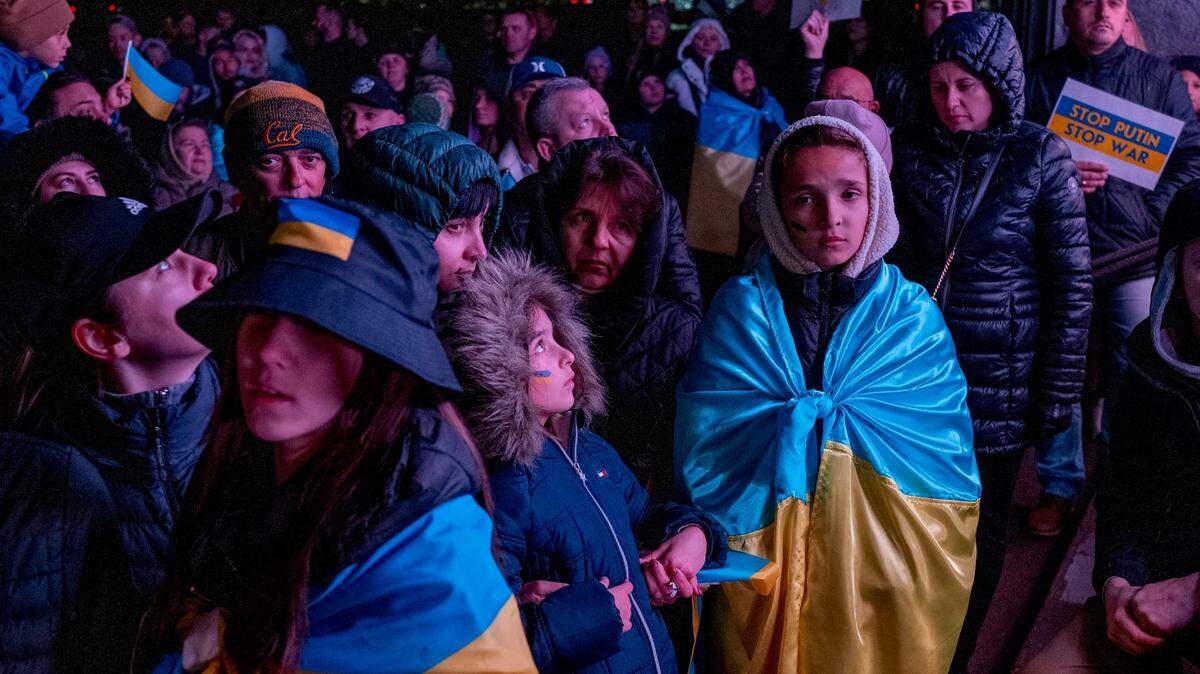 People draped in Ukrainian flags watch images from the war in Ukraine at the state Capitol on Friday, Feb. 24, 2023, as hundreds participated in a rally to mark the one year anniversary of the Russian invasion of the country.

