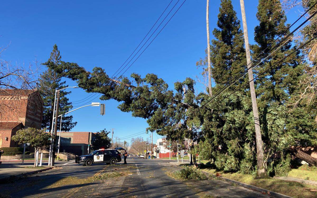A Sacramento police officer directs traffic near a tree suspended on power lines on Sunday at 39th and J streets near Sacred Heart Church. A New Year’s Eve storm brought high winds and heavy rain to the region, knocking out power for tens of thousands of people.