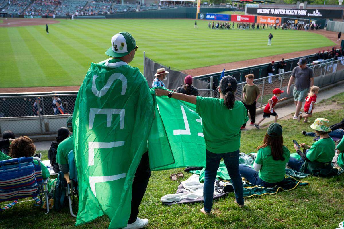 Last Dive Bar co-founder Bryan Johansen, left, wears a “SELL” flag during a protest Saturday at the River Cats game against the Las Vegas Aviators at Sutter Health Park.