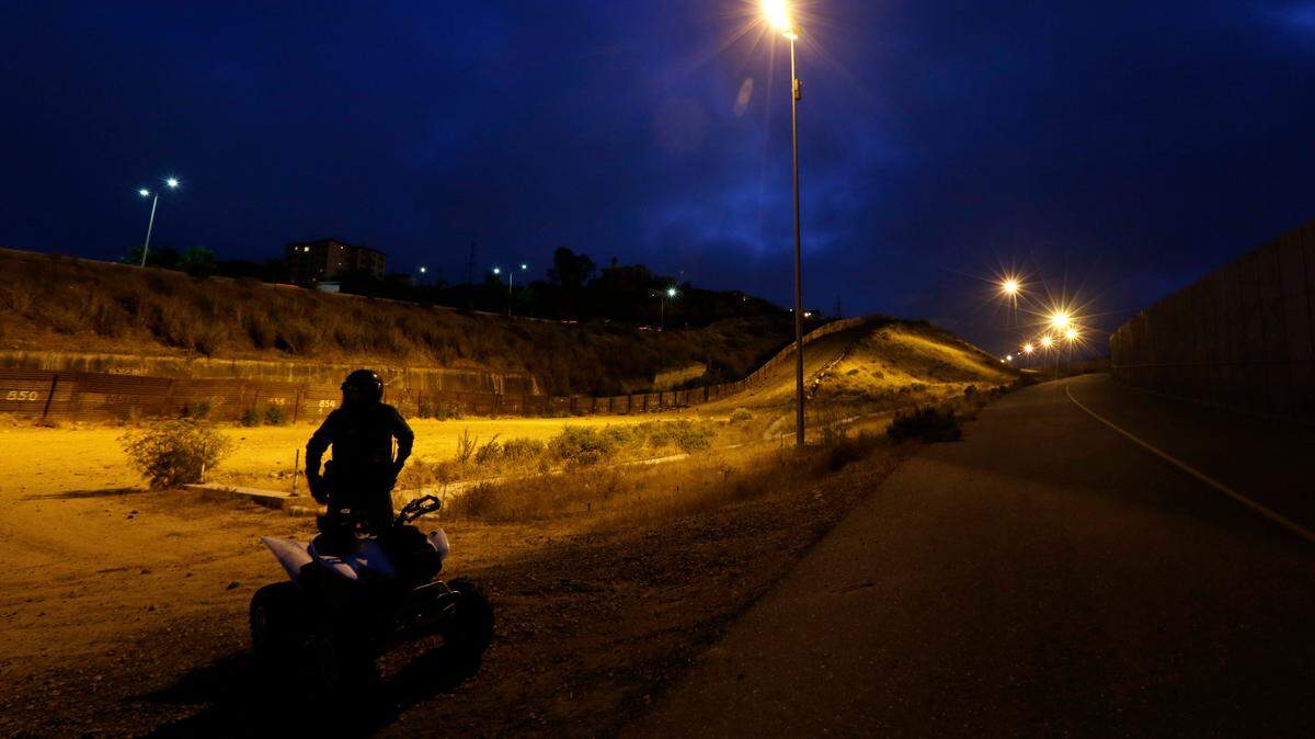 A U.S. Border Patrol agent rides an ATV as he patrols at night between the border structures separating Tijuana, Mexico, left, from San Diego in 2009. A man struck a Border Patrol agent with a rock and stole his ATV early Sunday before being shot, authorities say.