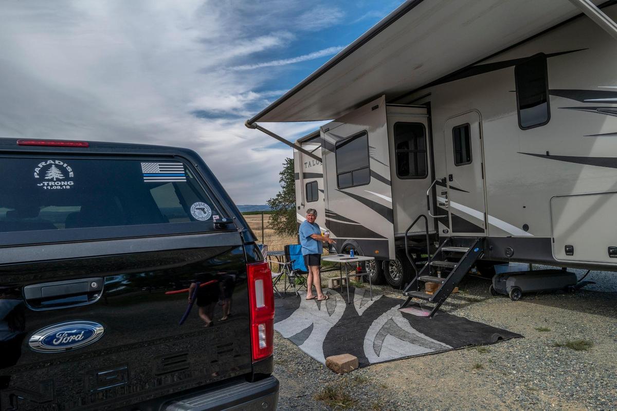Teri Lindsay stands outside in Oroville on Wednesday, June 1, 2022, between her rented travel trailer and her vehicle. She’s worried she will have to move from the trailer to the vehicle if she doesn’t receive a payment on time from the Fire Victims Trust, compensation for the loss of her home in the Camp Fire in 2018.