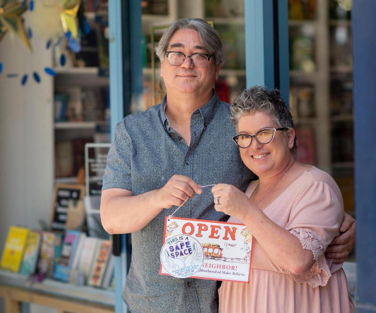 Ross and Heidi Rojek, owners of Capital Books on K Street in downtown Sacramento, pose for a portrait with their open sign May 28. They were one of the few businesses that stayed open on K Street during the shutdown, offering curbside service for their customers.