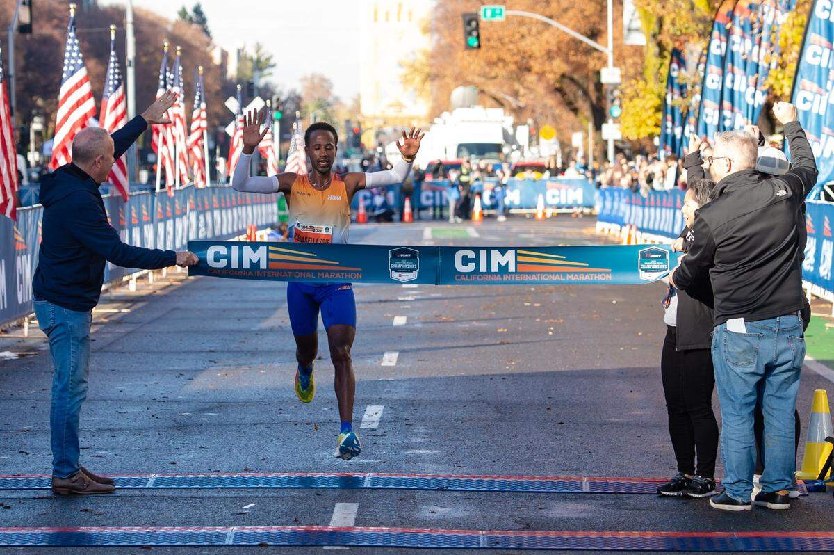 Futsum Zienasellassie crosses the finish line as Mayor Darrell Steinberg, left, holds the banner in the 2022 California International Marathon from Folsom to the state Capitol in downtown Sacramento on Dec. 4, 2022. Zienasellassie finished first overall.