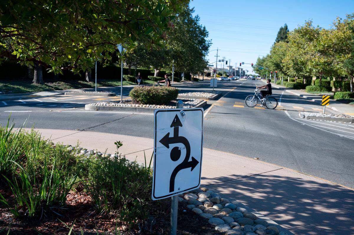 Young men ride their bikes through a crosswalk in an intersection with a roundabout designed to slow traffic by a school in Natomas on Monday, Aug. 19, 2024.