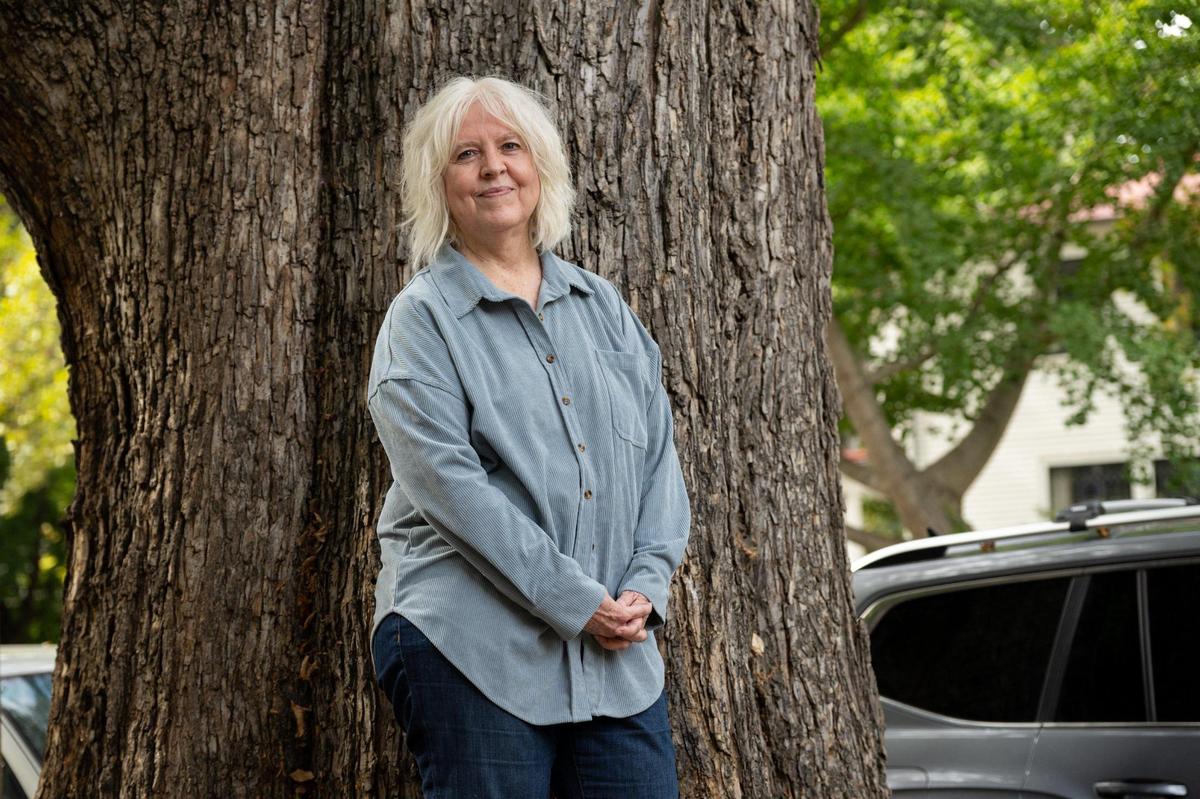 Susan Christian stands earlier this month in front of the trunk of the California elm tree that she wants to save on her property in Sacramento’s Boulevard Park. The city is considering cutting down the tree for safety, but an arborist hired by Christian believes that only part of it needs to be removed.