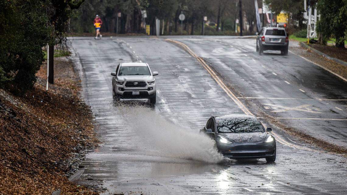 A Tesla, without a front license plate, crosses a flooded section of Sutterville Road in Sacramento on Tuesday, Dec. 27, 2022.